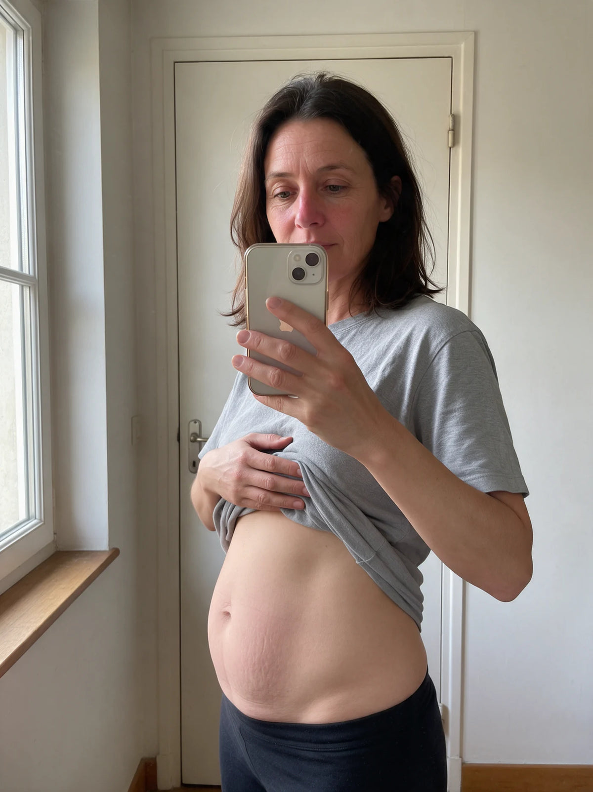 Une femme observe son ventre dans le miroir de sa chambre